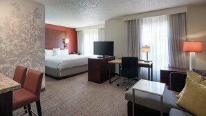 A hotel room with a bed, a desk with a computer, a television, and a seating area with a couch and chairs.