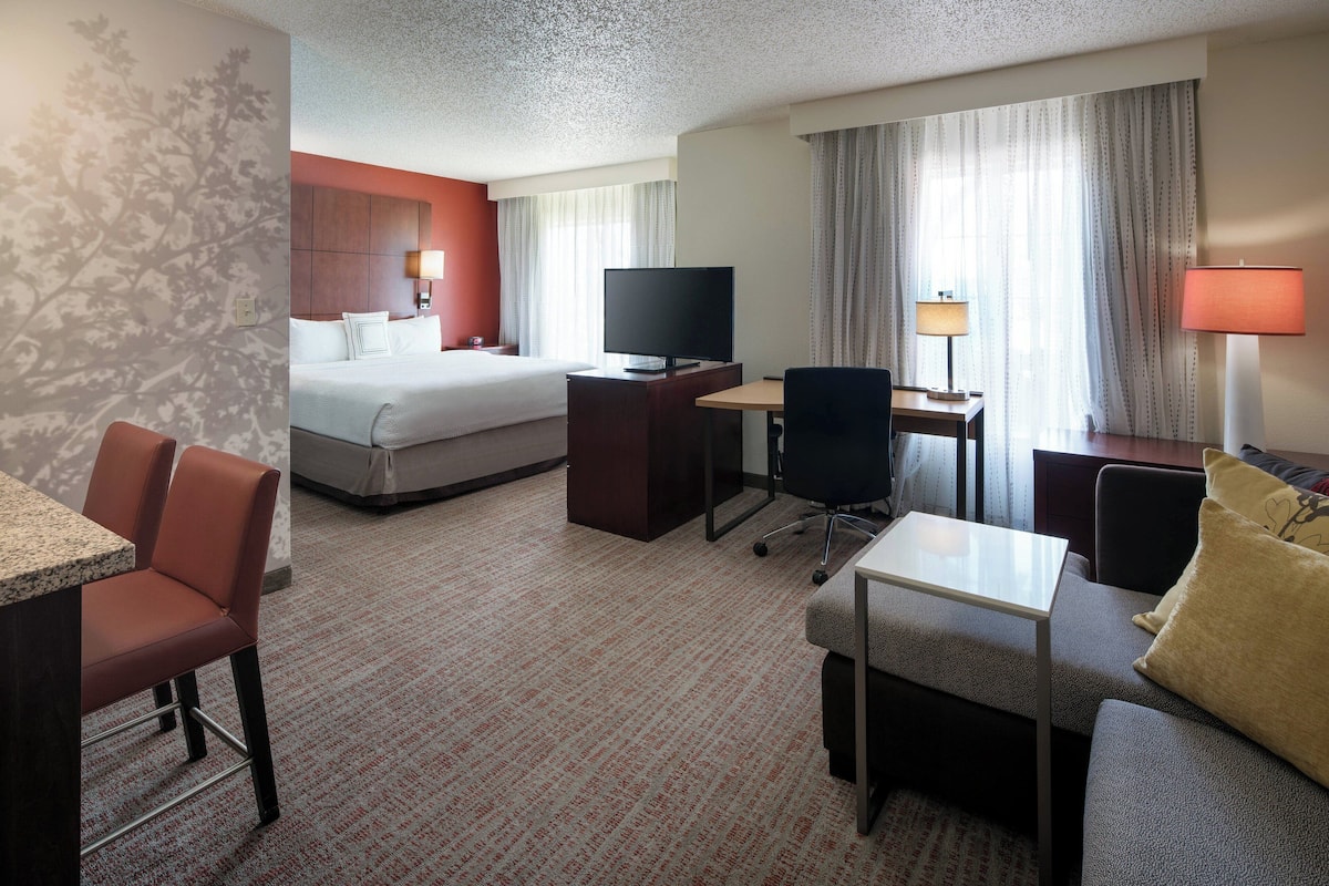 A hotel room with a bed, a desk with a computer, a television, and a seating area with a couch and chairs.