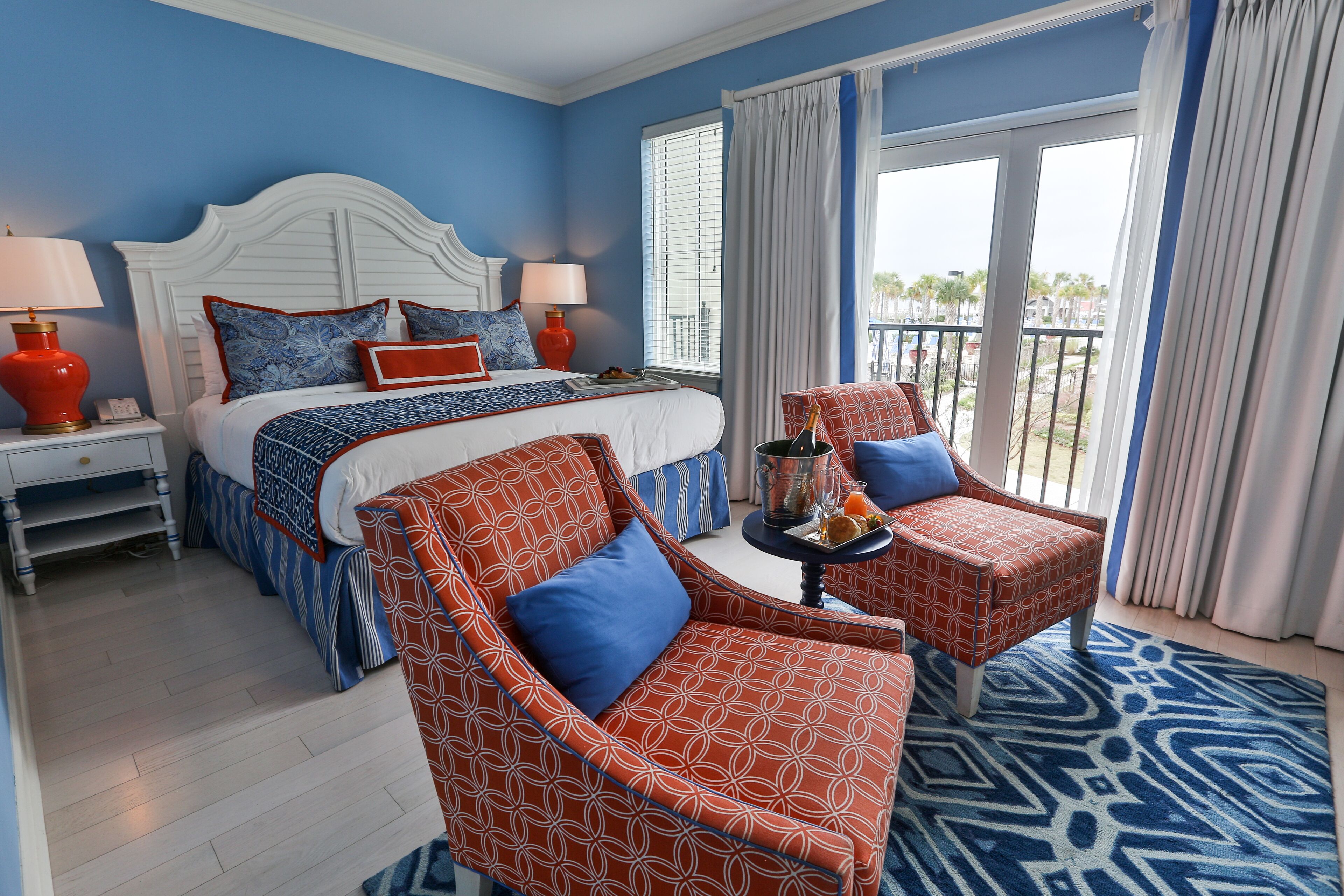 A hotel room with a bed, two armchairs, a nightstand, a lamp, and a view of the outdoors.