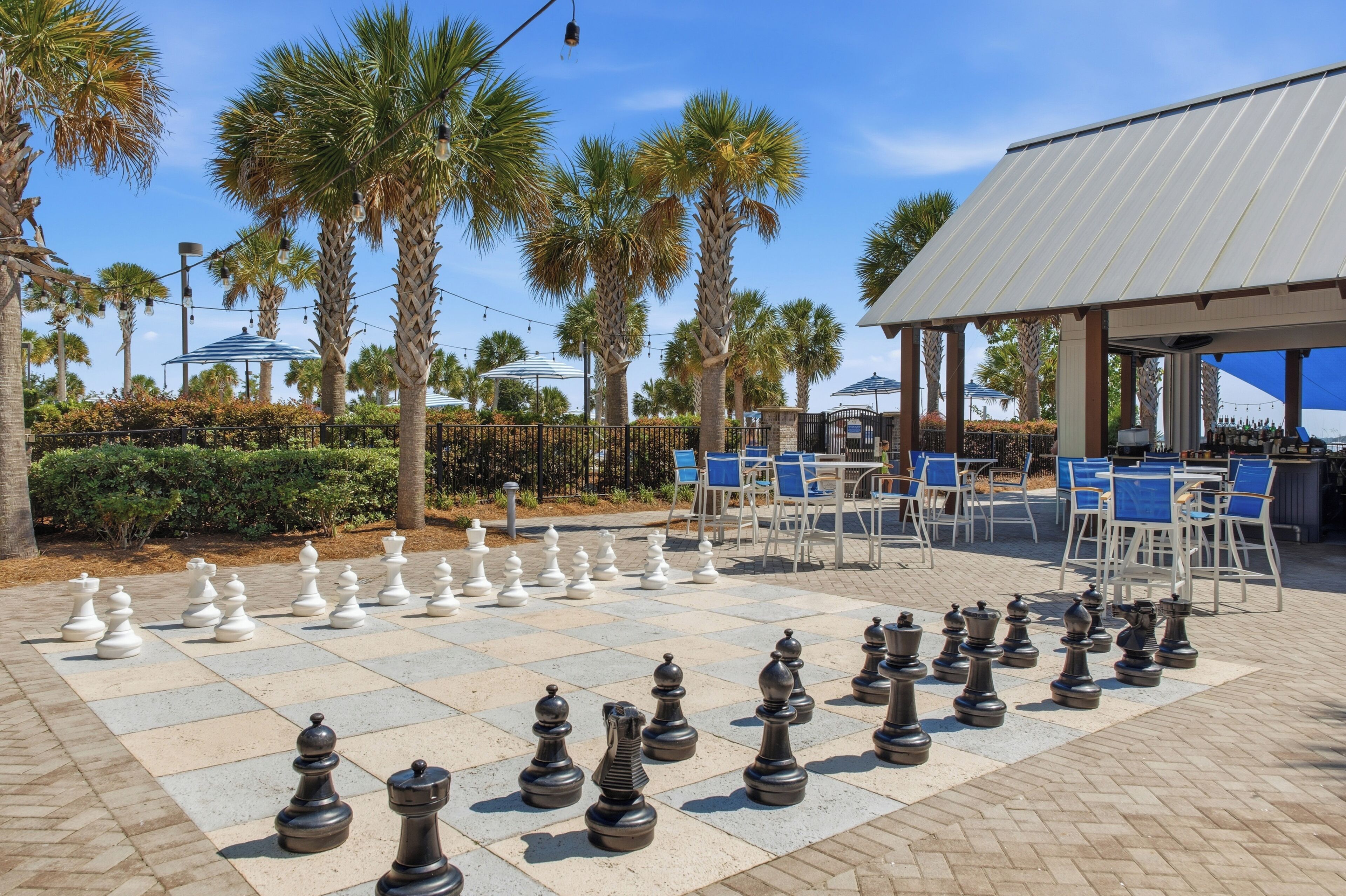 A chessboard set up outdoors with palm trees and a covered seating area in the background.