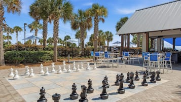 A chessboard set up outdoors with palm trees and a covered seating area in the background.