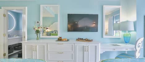 A bedroom with a bed, a dresser, a vanity, and a TV.