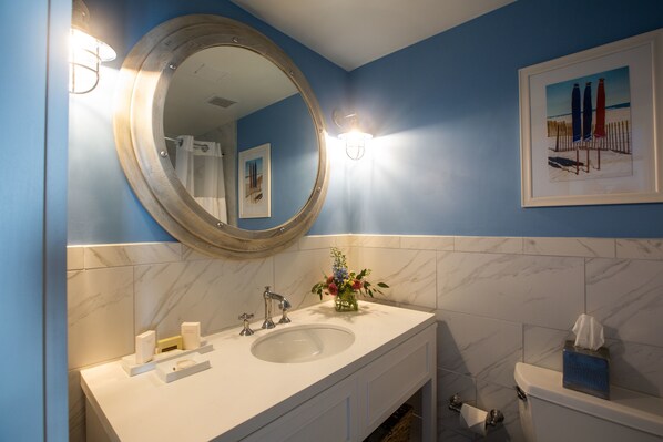 A bathroom with a large round mirror, a sink, and a toilet. There is a framed picture on the wall and a vase with flowers on the sink. - Harborside at Charleston Harbor Resort and Marina (Mount Pleasant)