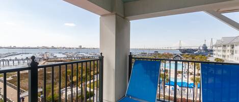 A balcony with a view of a marina, a swimming pool, and a distant bridge.