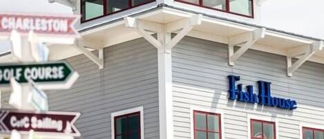 Un edificio con un letrero que dice "Fish House" y varios carteles que señalan lugares cercanos como Charleston, un campo de golf y un club de vela.