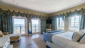 Habitación de hotel con una cama grande, una zona de estar con mesa y sillas, un televisor de pantalla plana y un balcón con vistas al mar.