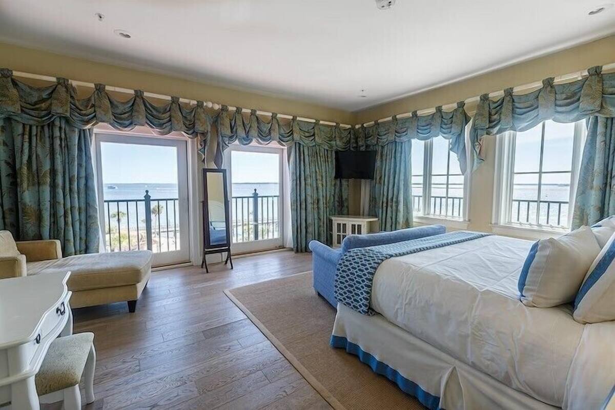 Ein Hotelzimmer mit einem großen Bett, einer Sitzecke mit Tisch und Stühlen, einem Flachbildfernseher und einem Balkon mit Meerblick.