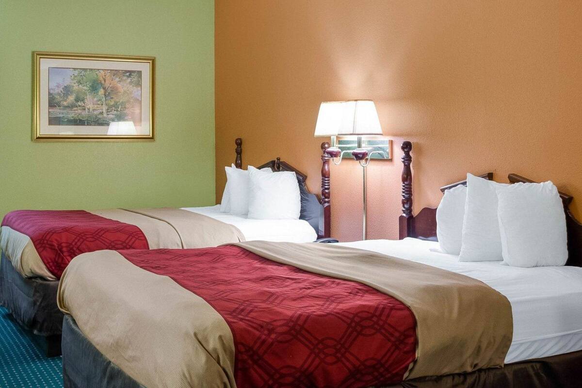 A hotel room with two beds, a painting on the wall, and a lamp between the beds.