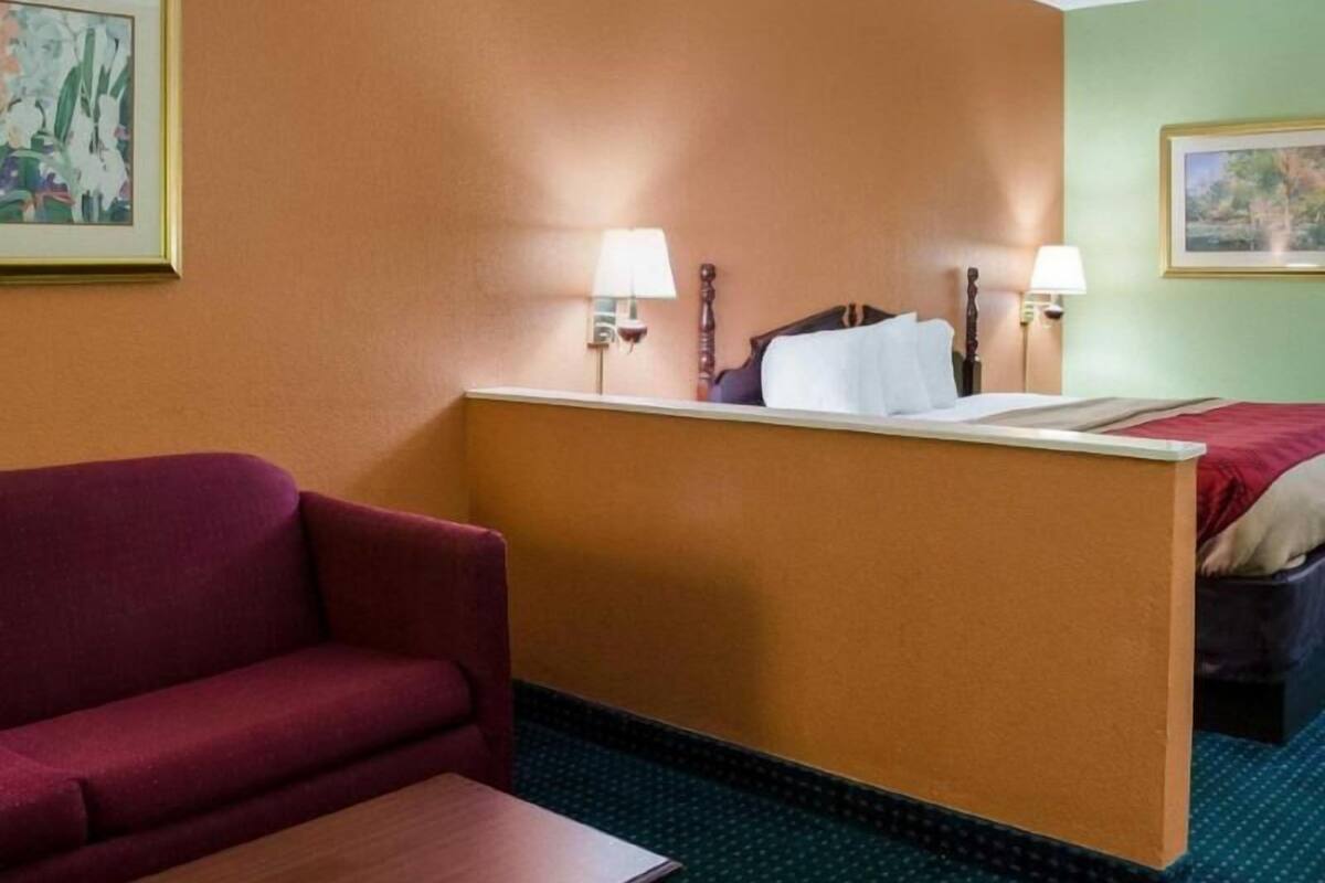 A hotel room with a single bed, a desk, a chair, a sofa, and two wall-mounted lamps.