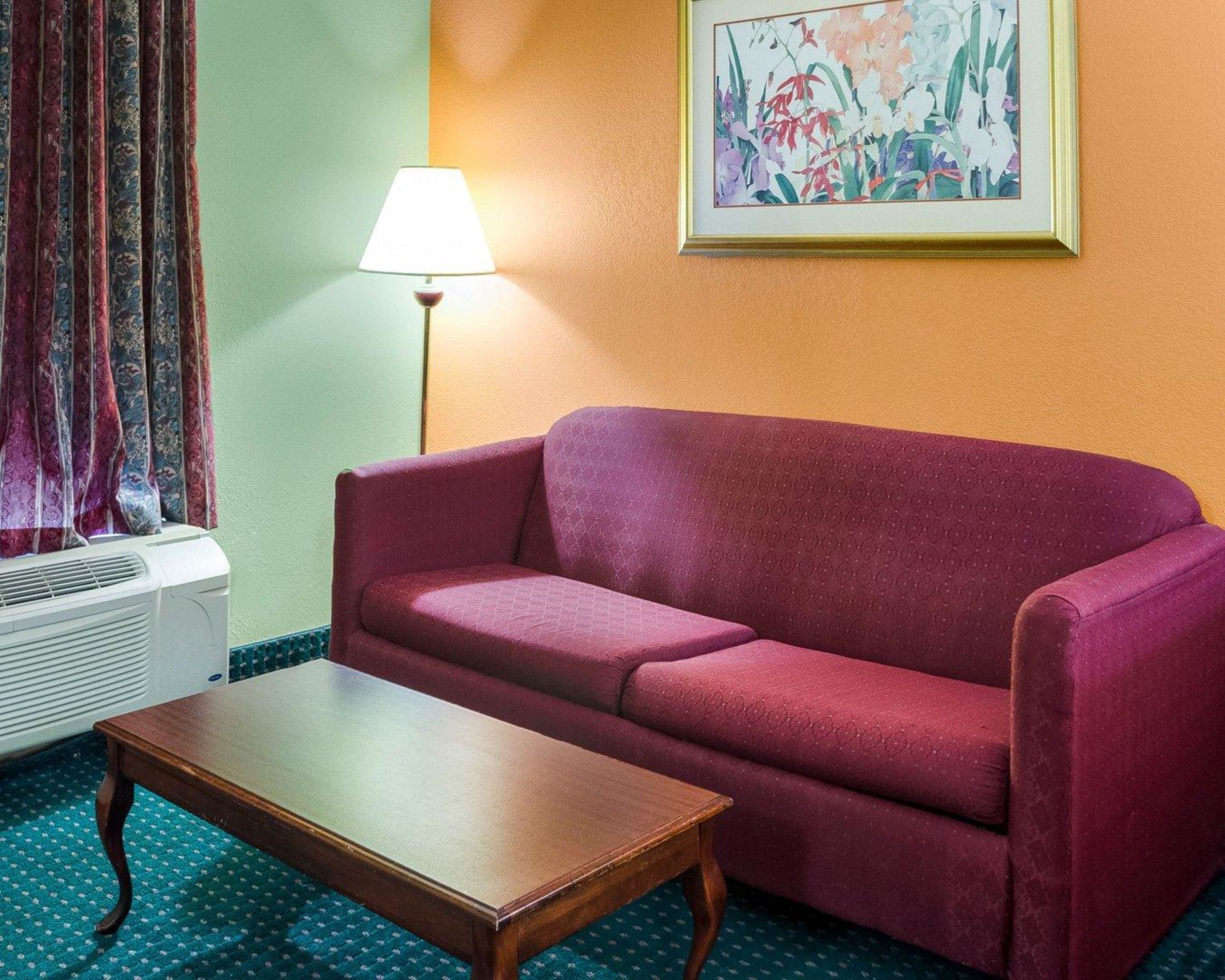 A room with a red sofa, a wooden coffee table, a floor lamp, and a painting on the wall.