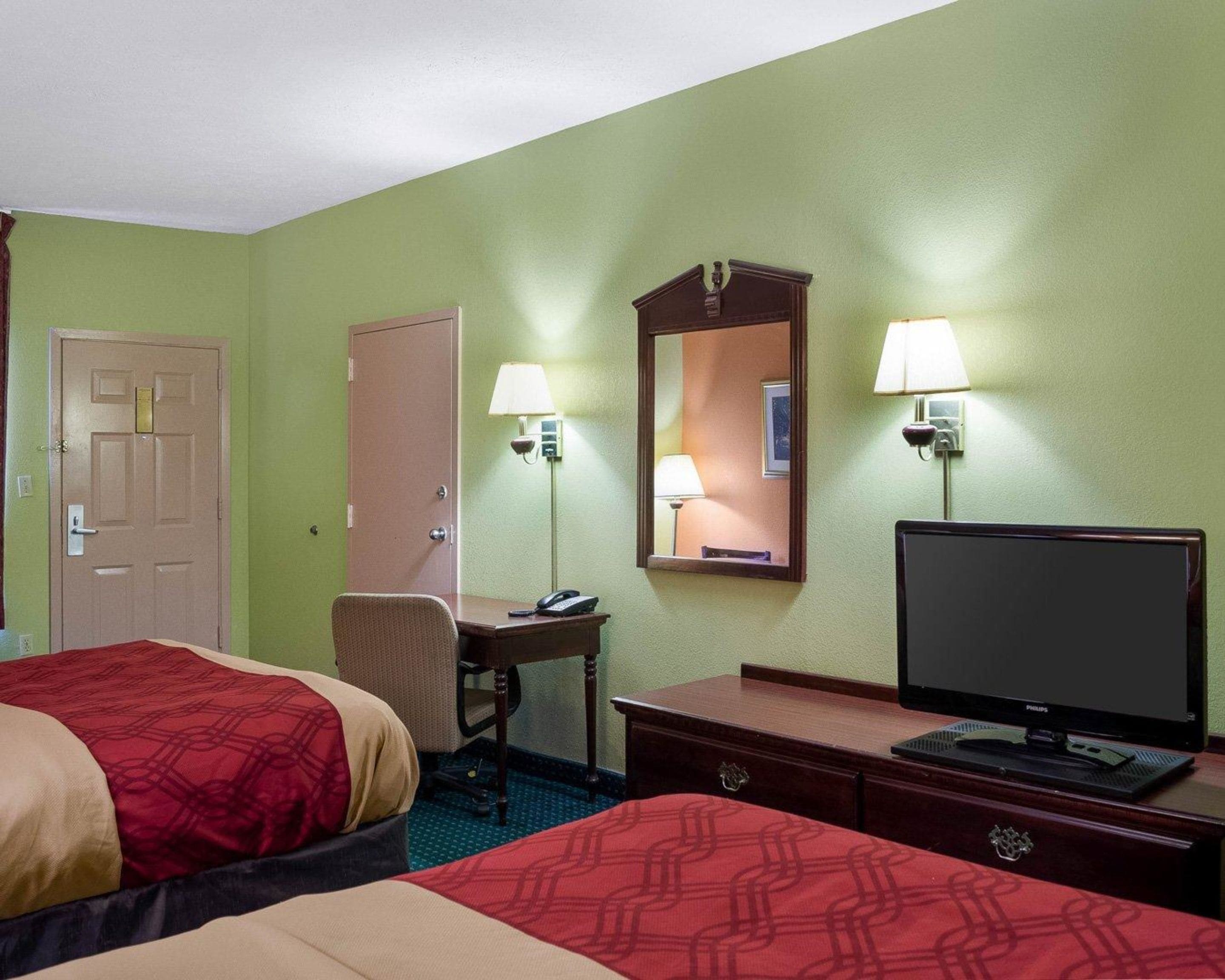 A hotel room with two beds, a desk with a lamp, a television, and a mirror.