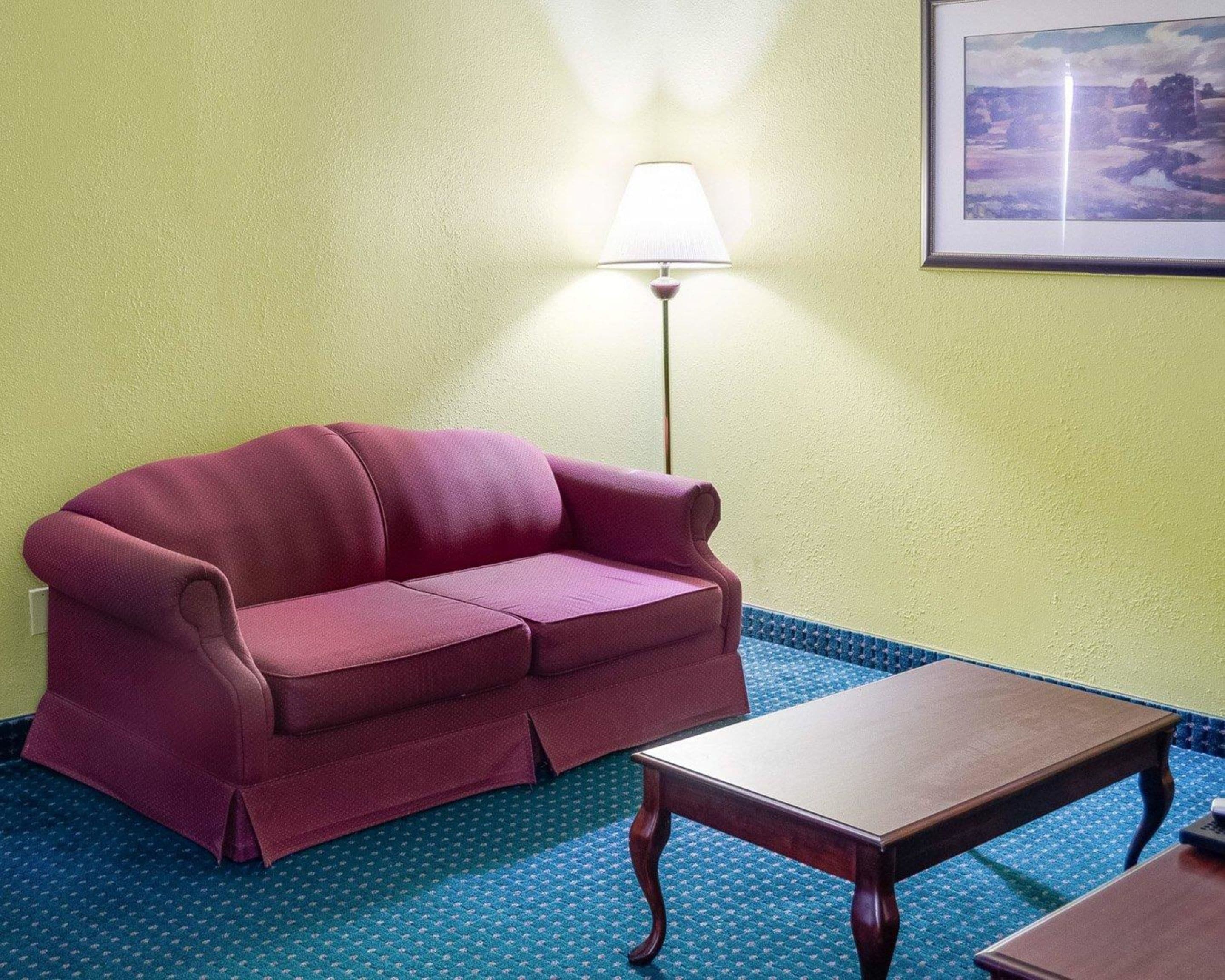 A room with a red sofa, a wooden table, a lamp, and a framed picture on the wall.