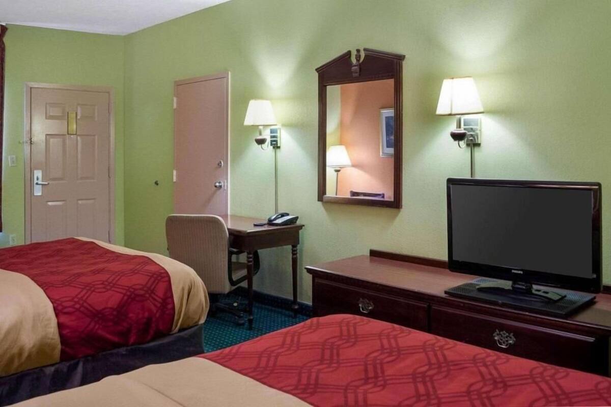 A hotel room with two beds, a desk with a lamp, a television, and a door.