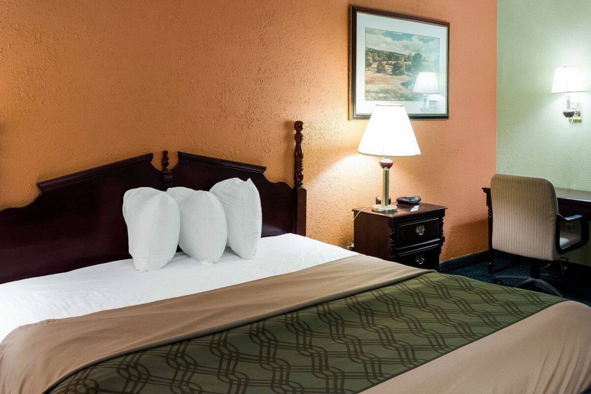 A hotel room with a bed, a nightstand with a lamp, a chair, and a framed picture on the wall.