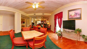 A dining area with a wooden table and chairs, a ceiling fan, and a television on a stand.
