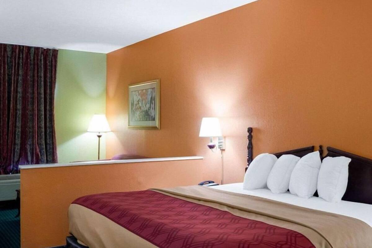 A hotel room with a bed, two bedside lamps, a painting on the wall, and a window with curtains.