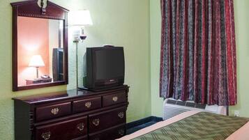 A hotel room with a bed, a dresser with drawers, a television on top of the dresser, a mirror on the wall, a lamp, and a window with curtains.