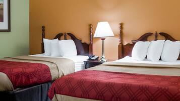 A hotel room with two beds, each with a wooden headboard, a bedside table with a lamp, and a framed picture on the wall.