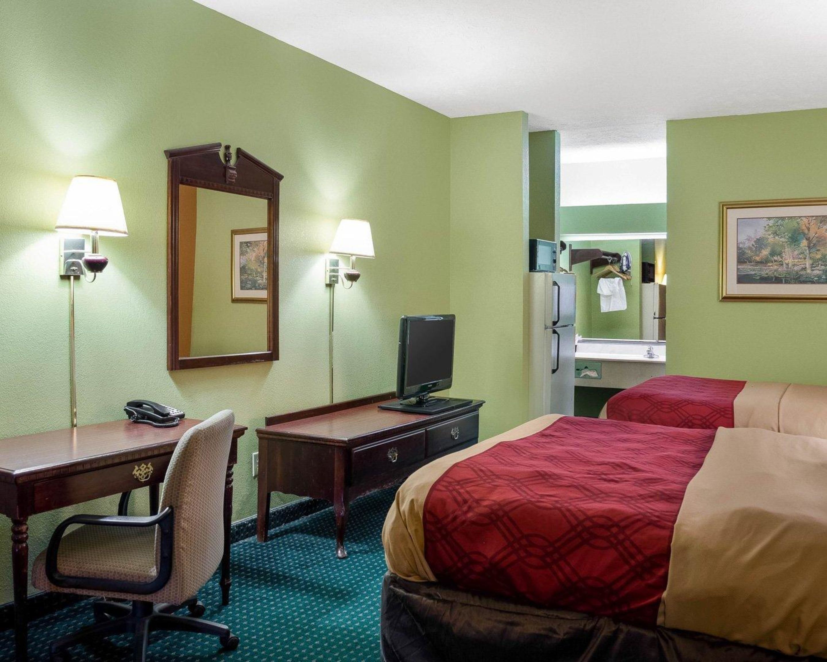Una habitación de hotel con escritorio, dos camas, televisor, espejo y refrigerador.