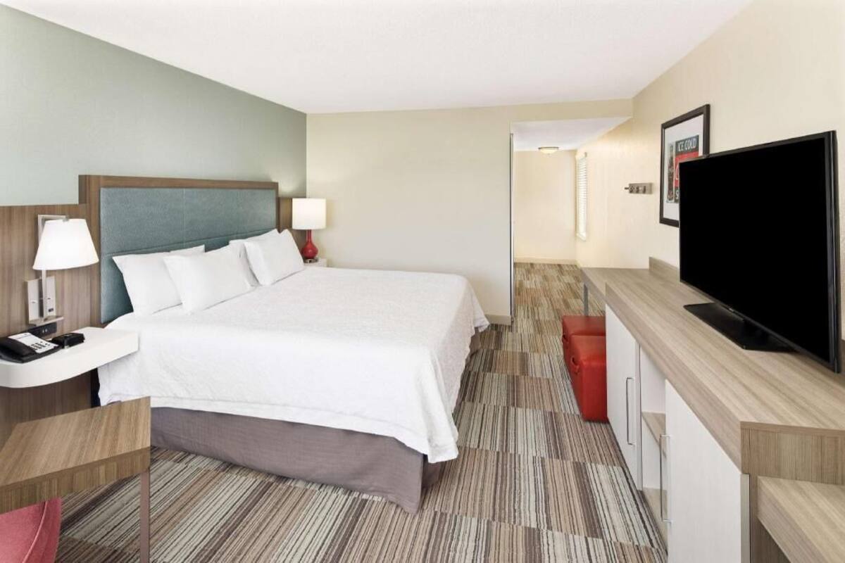 A hotel room with a bed, bedside tables, a TV, and a desk area.