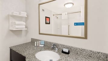 A bathroom with a granite countertop sink, a mirror, a towel rack with folded towels, a framed picture on the wall, and a sign with directional arrows.