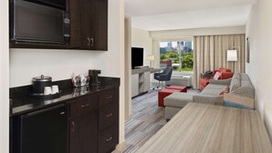 A compact hotel room with a kitchenette, a sofa, a TV, and a view of the city.