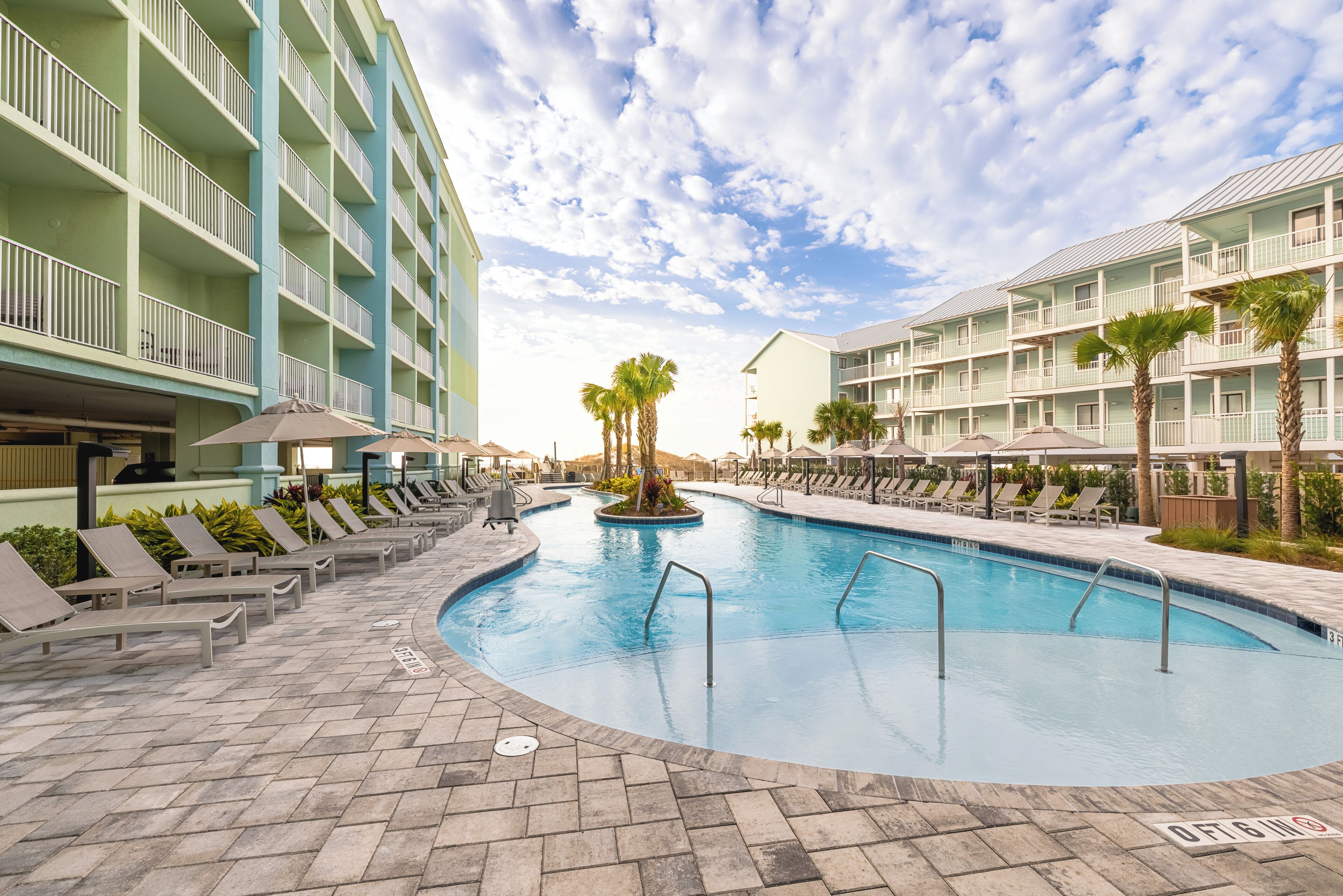 A pool area with lounge chairs and umbrellas, surrounded by multi-story buildings with balconies.
