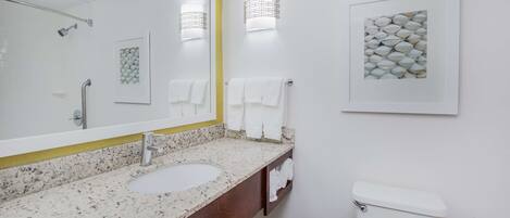 Un baño con lavamanos de encimera de granito, un espejo grande, un inodoro blanco y dos luces empotradas.