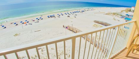Vista a la playa desde un balcón con barandilla de madera, una playa de arena y un cielo azul despejado.