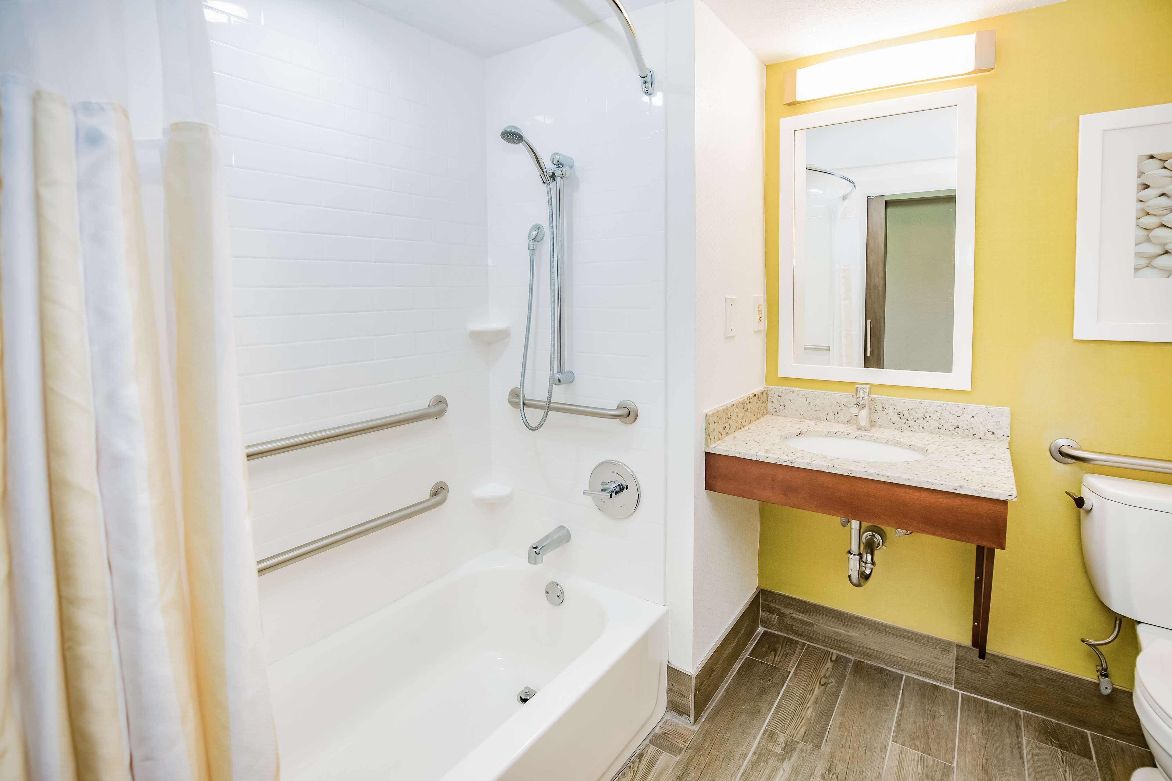A bathroom with a bathtub, shower, and sink. There are grab bars and a mirror above the sink.