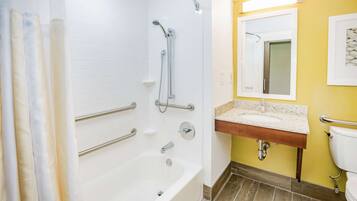 A bathroom with a bathtub, shower, and sink. There are grab bars and a mirror above the sink.