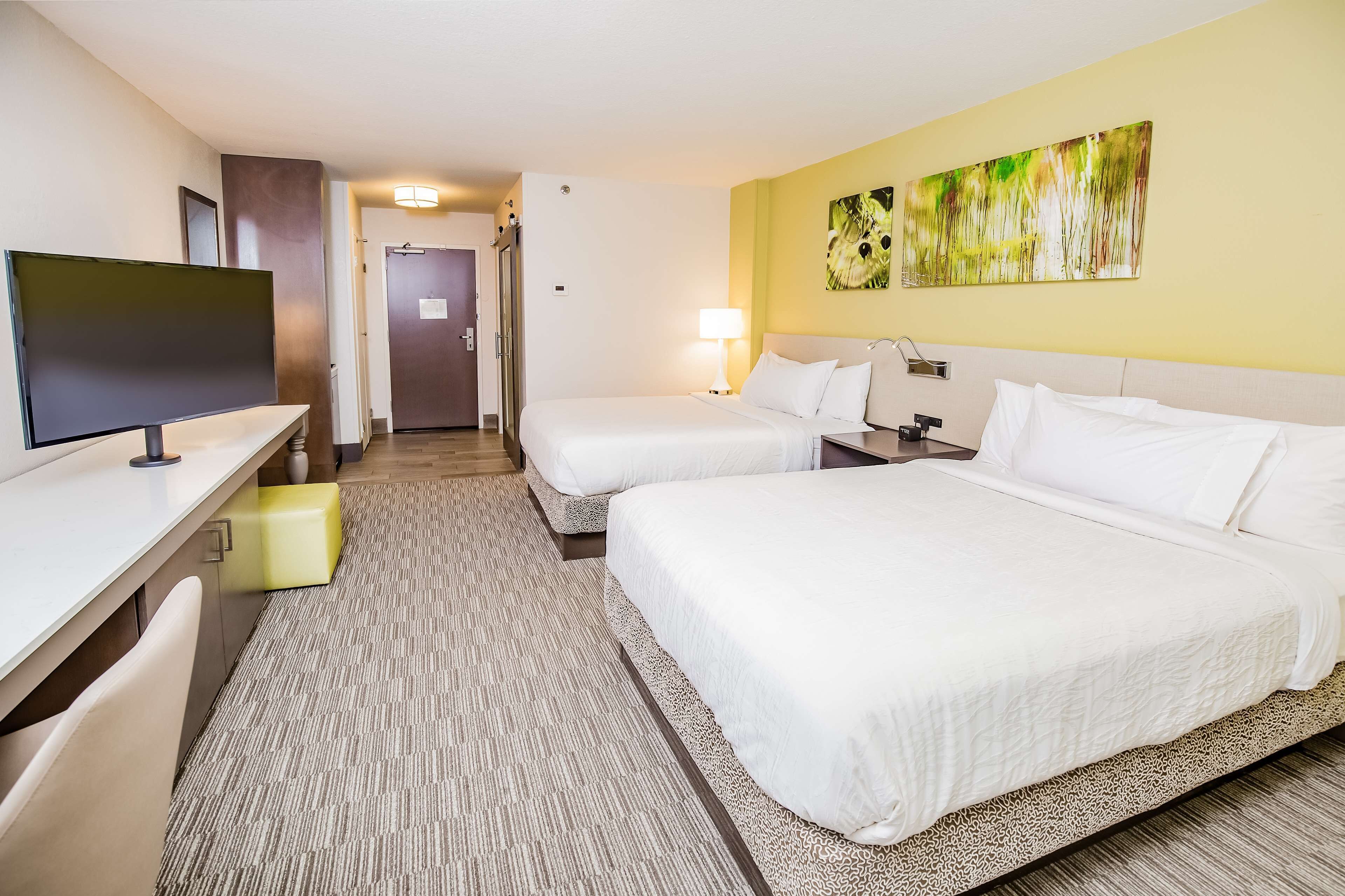 A hotel room with two beds, a desk, a television, and a painting on the wall.
