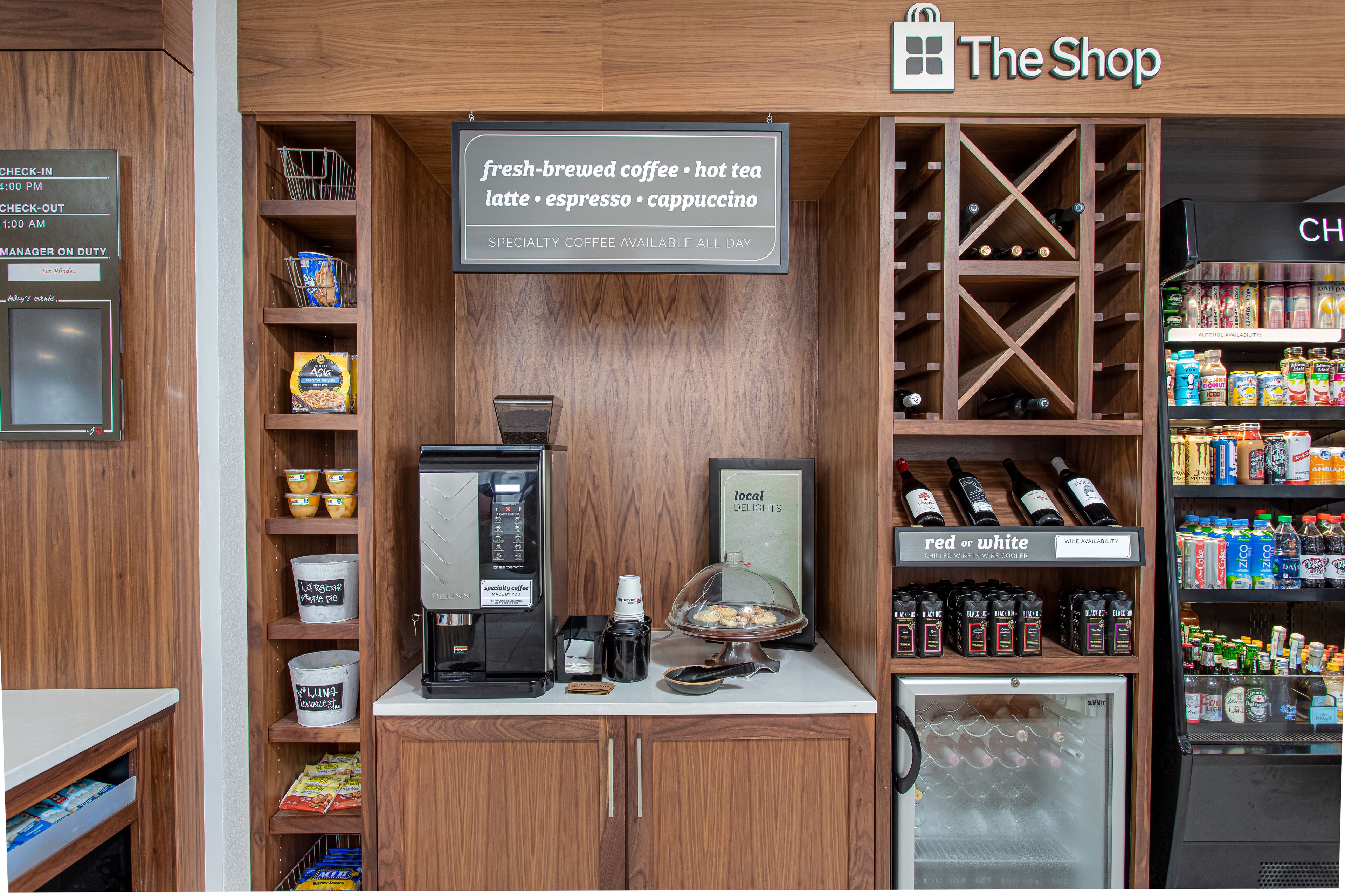 A coffee shop with a coffee machine, a display of local delights, and a wine cooler.