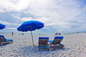 A beach with blue umbrellas and wooden lounge chairs.