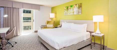 Habitación de hotel con una cama grande, un escritorio, una silla, dos lámparas de noche y un cuadro en la pared.