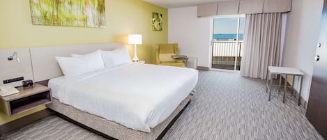 Habitación de hotel con una cama grande, una mesita de noche, un escritorio, una silla y un balcón con cortinas.