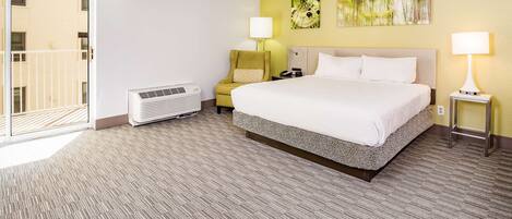 A hotel room with a large bed, a chair, a standing heater, and a view of the outside through a sliding door.