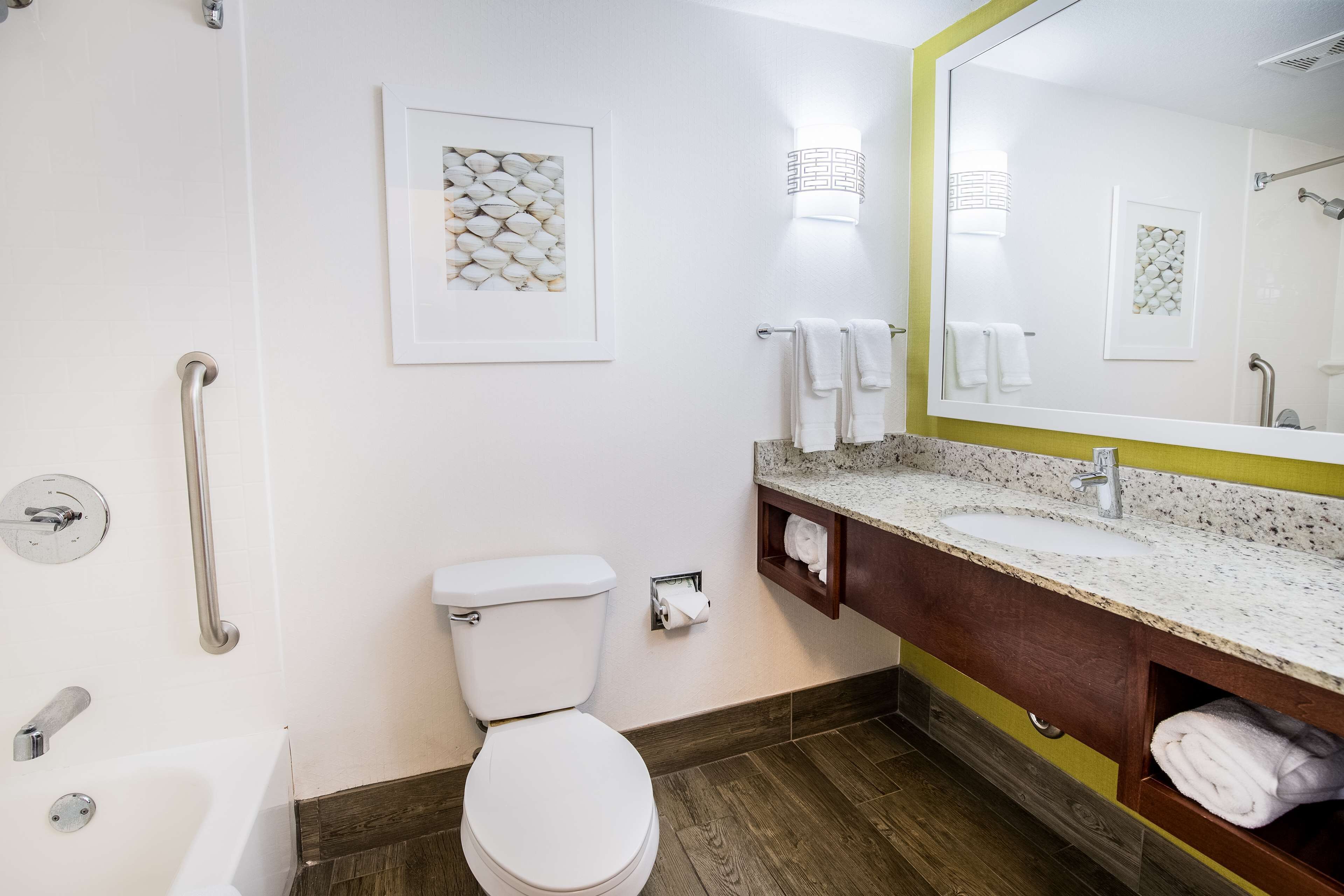 A bathroom with a white toilet, a sink with a granite countertop, a mirror with a yellow frame, and a shower area.