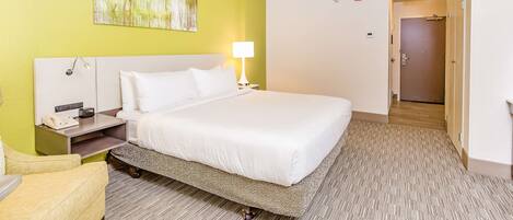 A hotel room with a bed, bedside table, lamp, and a painting on the wall.