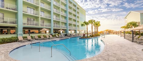 A hotel with a swimming pool, lounge chairs, and palm trees.