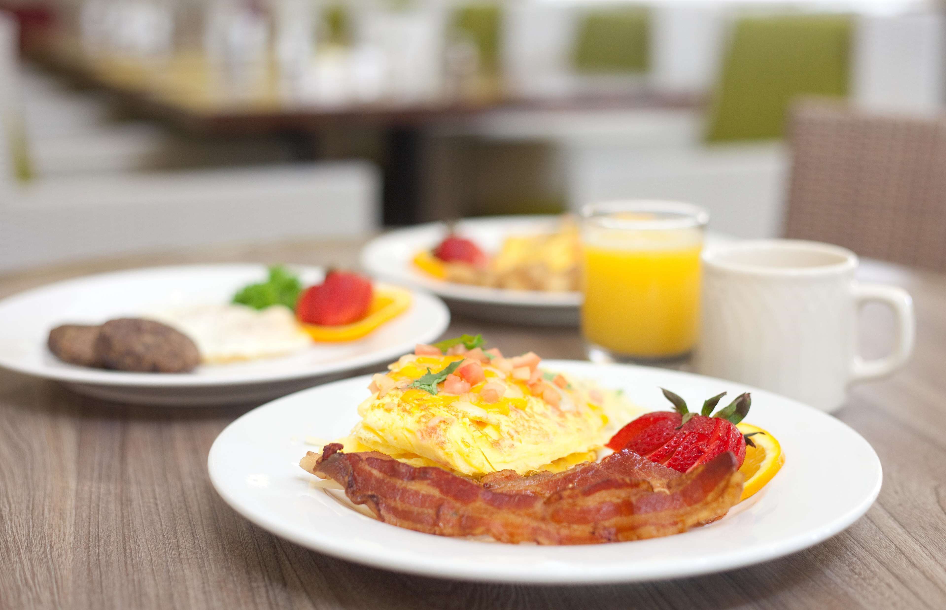 A breakfast setting with plates of food, including eggs, bacon, and fruit, and a glass of orange juice on a wooden table.