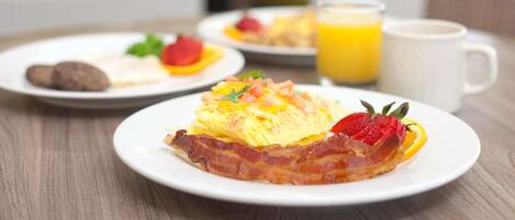 A breakfast setting with plates of food, including eggs, bacon, and fruit, and a glass of orange juice on a wooden table.