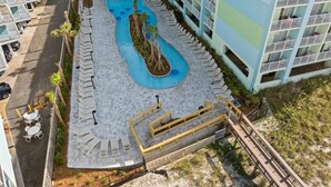 A pool area with lounge chairs, a wooden deck, and a building with balconies. - Hilton Garden Inn Orange Beach Beachfront (Orange Beach)