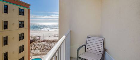 A balcony with a view of the beach and ocean, a pool, and a chair.