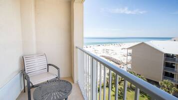 Un balcón con vista a una playa, una silla y una mesa.
