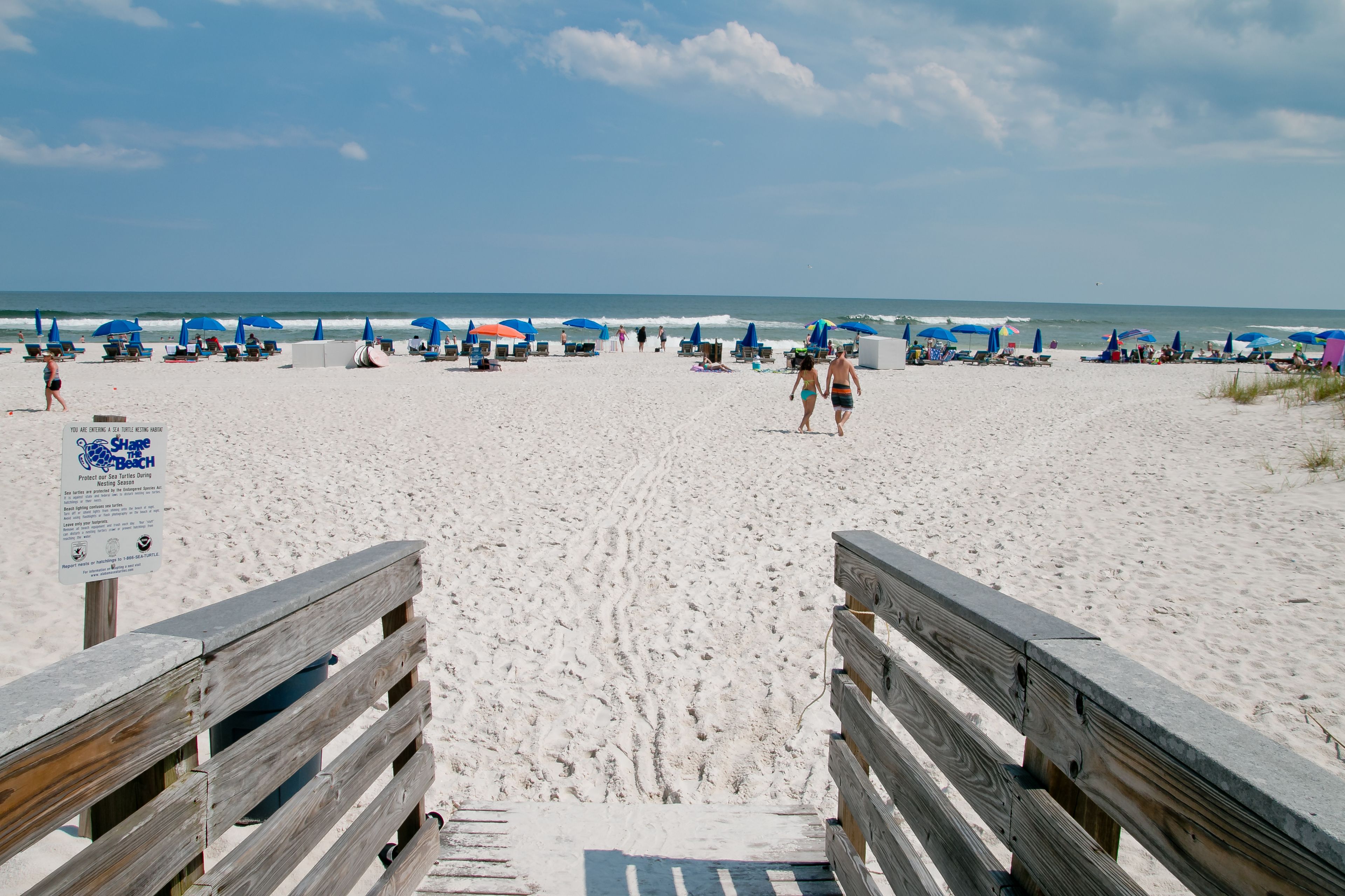 Une plage avec des passerelles en bois menant au bord de l’eau, des parasols et des chaises de plage.