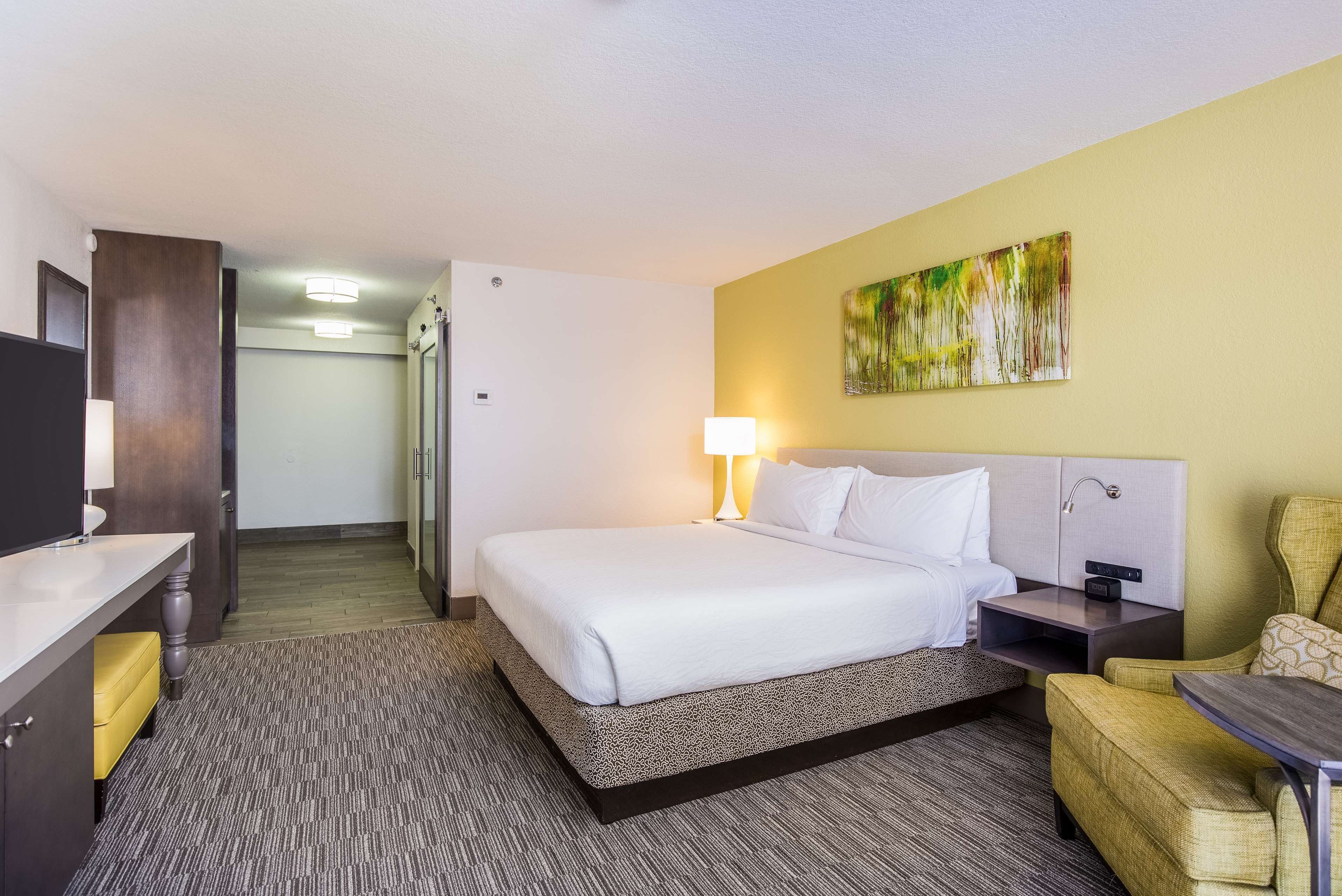 A hotel room with a bed, bedside table, lamp, and a chair.