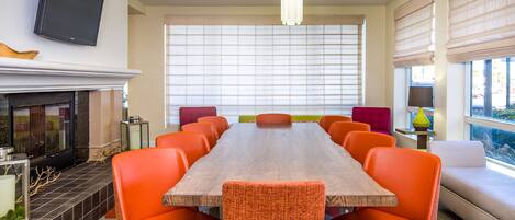 A conference room with a long table, orange chairs, a fireplace, and large windows with blinds.