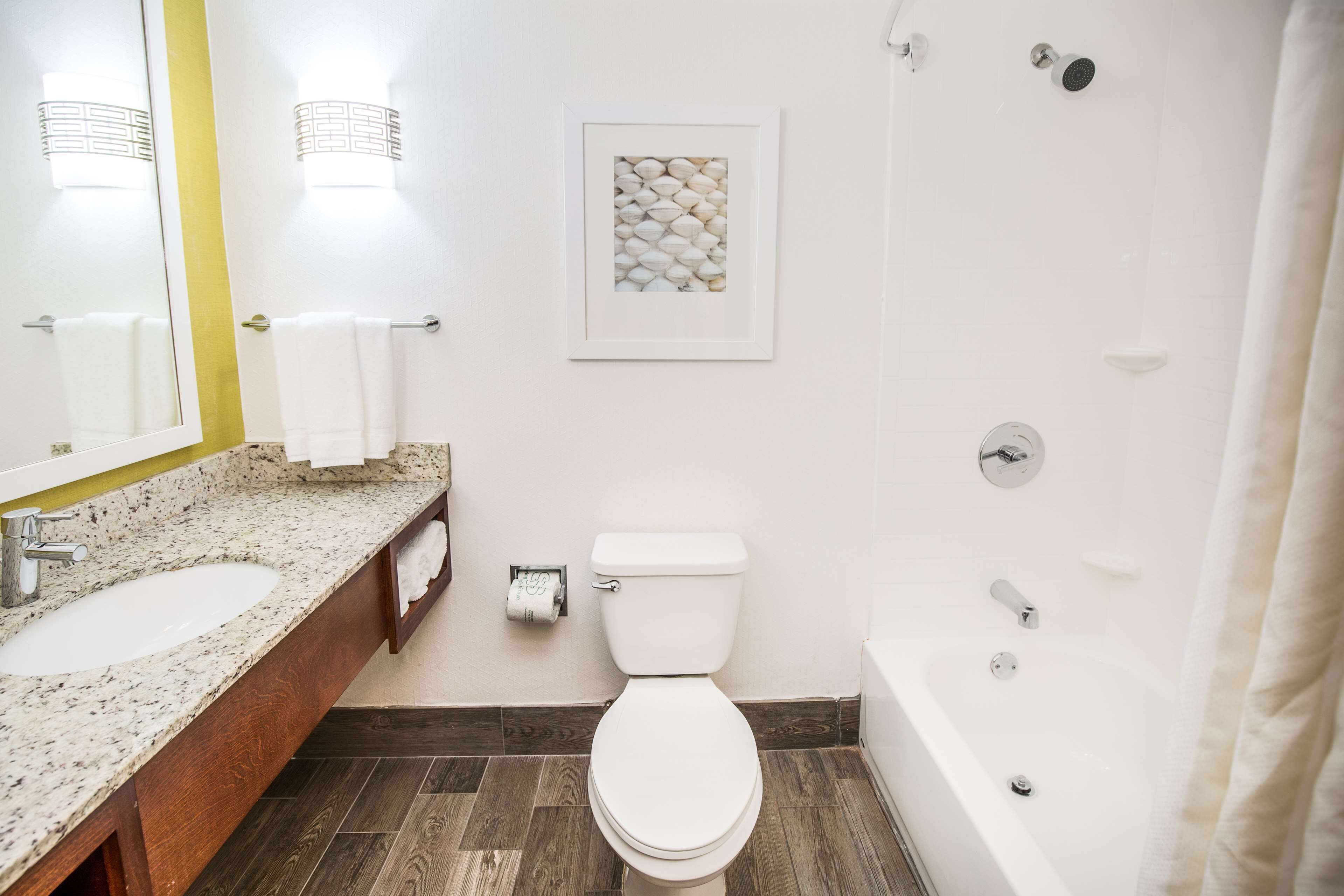 A bathroom with a white sink, toilet, and bathtub. There is a framed picture on the wall and a towel rack with towels.