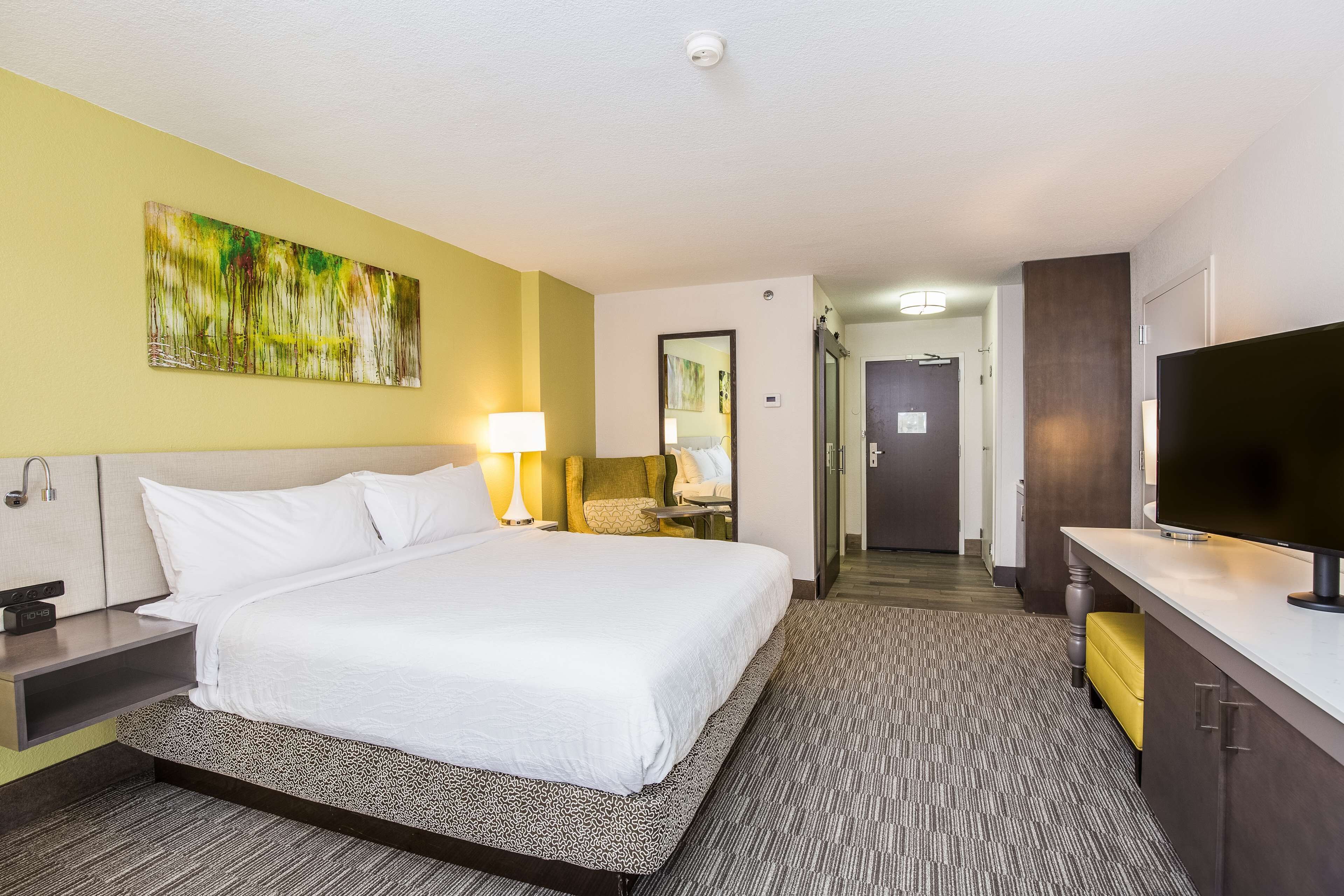 A hotel room with a large bed, bedside table, lamp, and a TV.